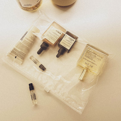 An open, transparent plastic bag filled with various small cosmetic samples, including bottles with pipettes, tubes, and an atomizer, lying on a light-colored, slightly shiny surface.